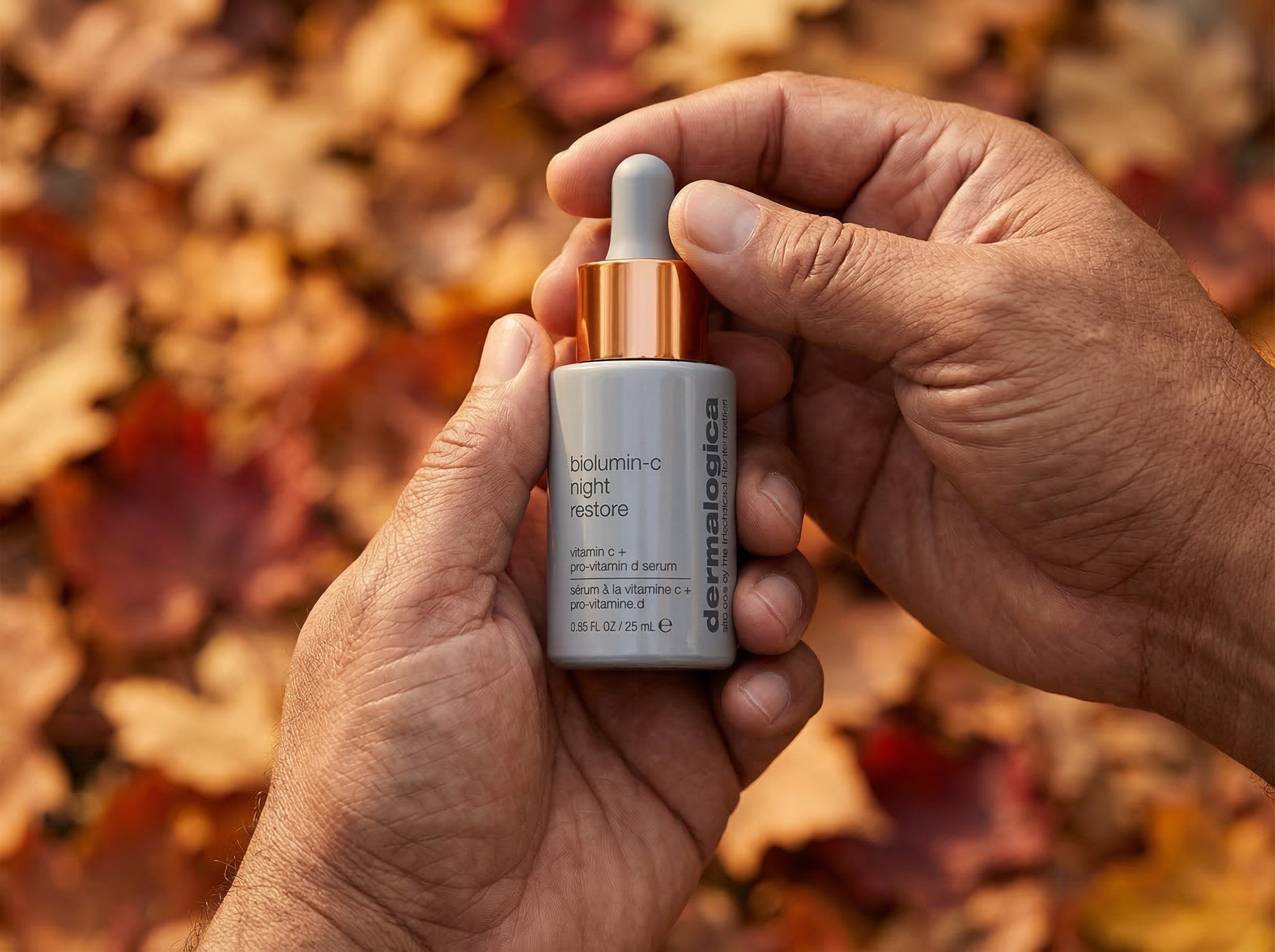 Hands holding Dermalogica BioLumin-C Serum bottle with autumn leaves in soft focus background