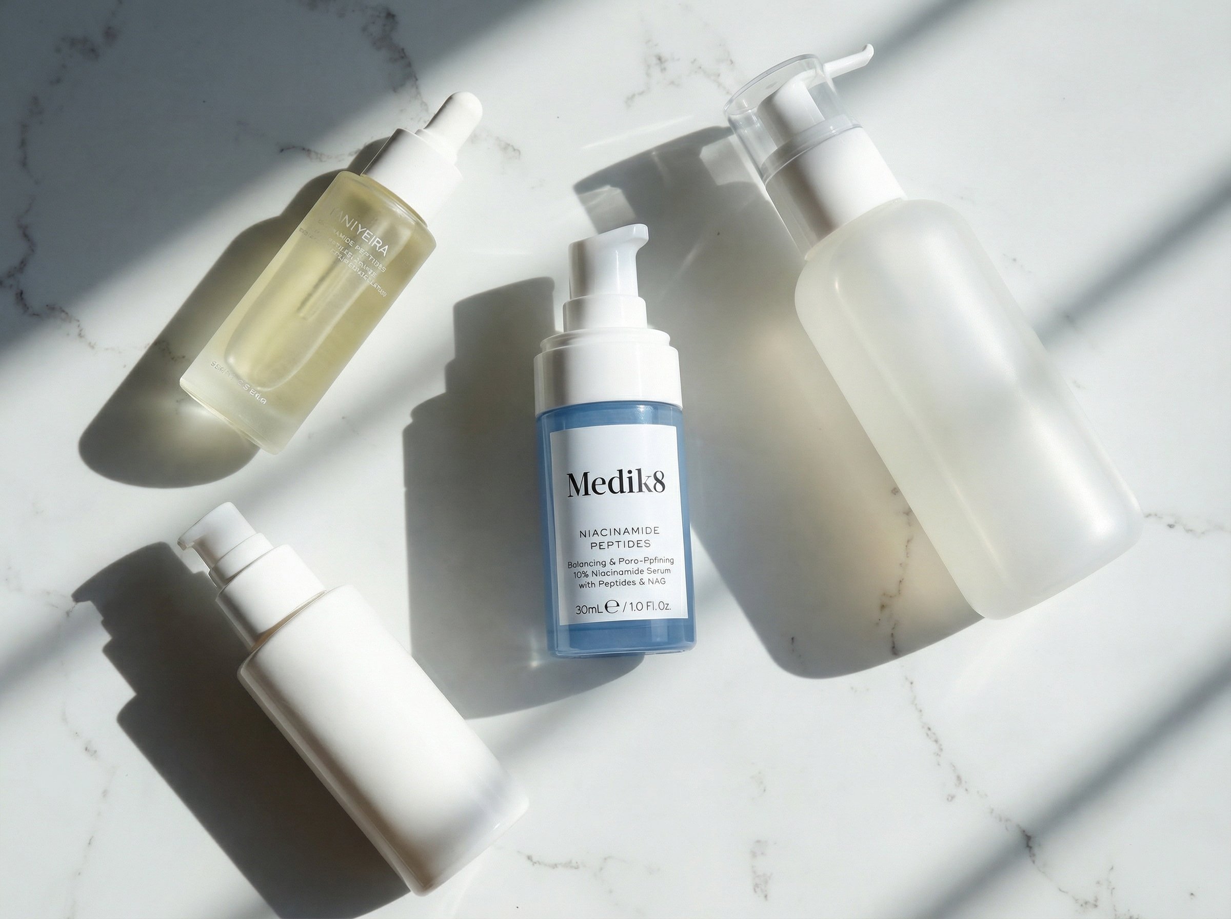 Flat lay of complete pigmentation skincare routine including niacinamide serum, vitamin C, SPF and cleanser on marble surface