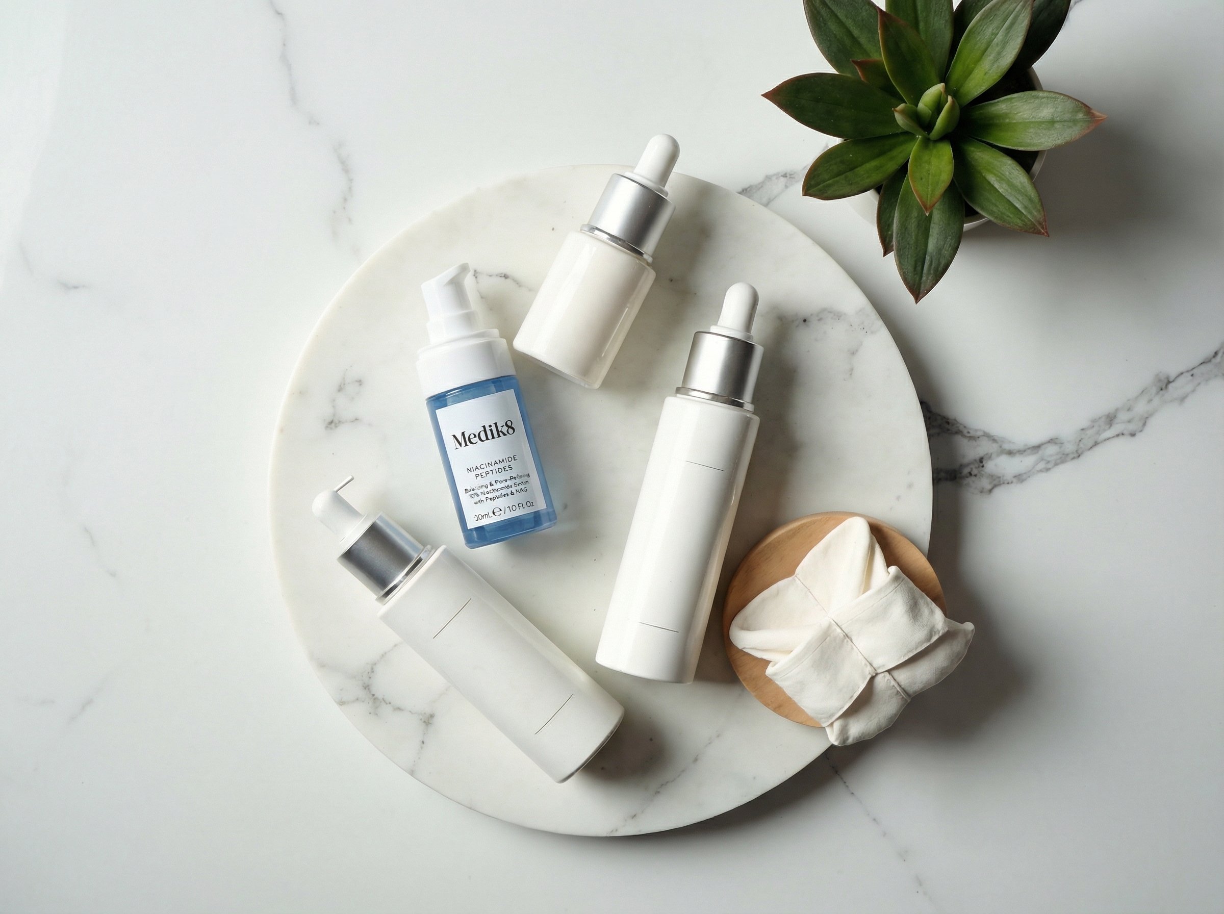 Overhead view of minimal skincare routine with three serum bottles on marble surface in natural lighting
