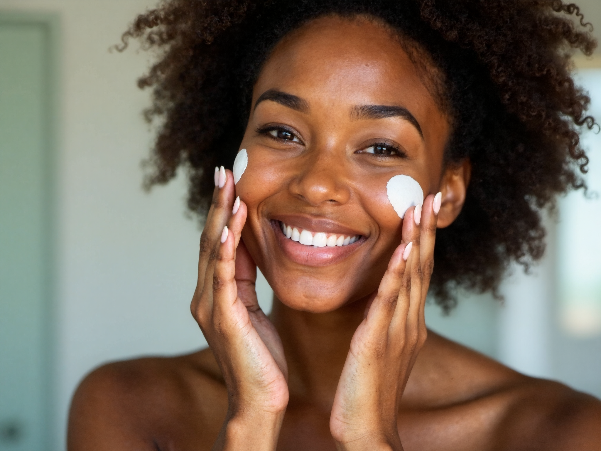 Young woman in her twenties applying facial cream in bright morning light, demonstrating preventive skincare routine