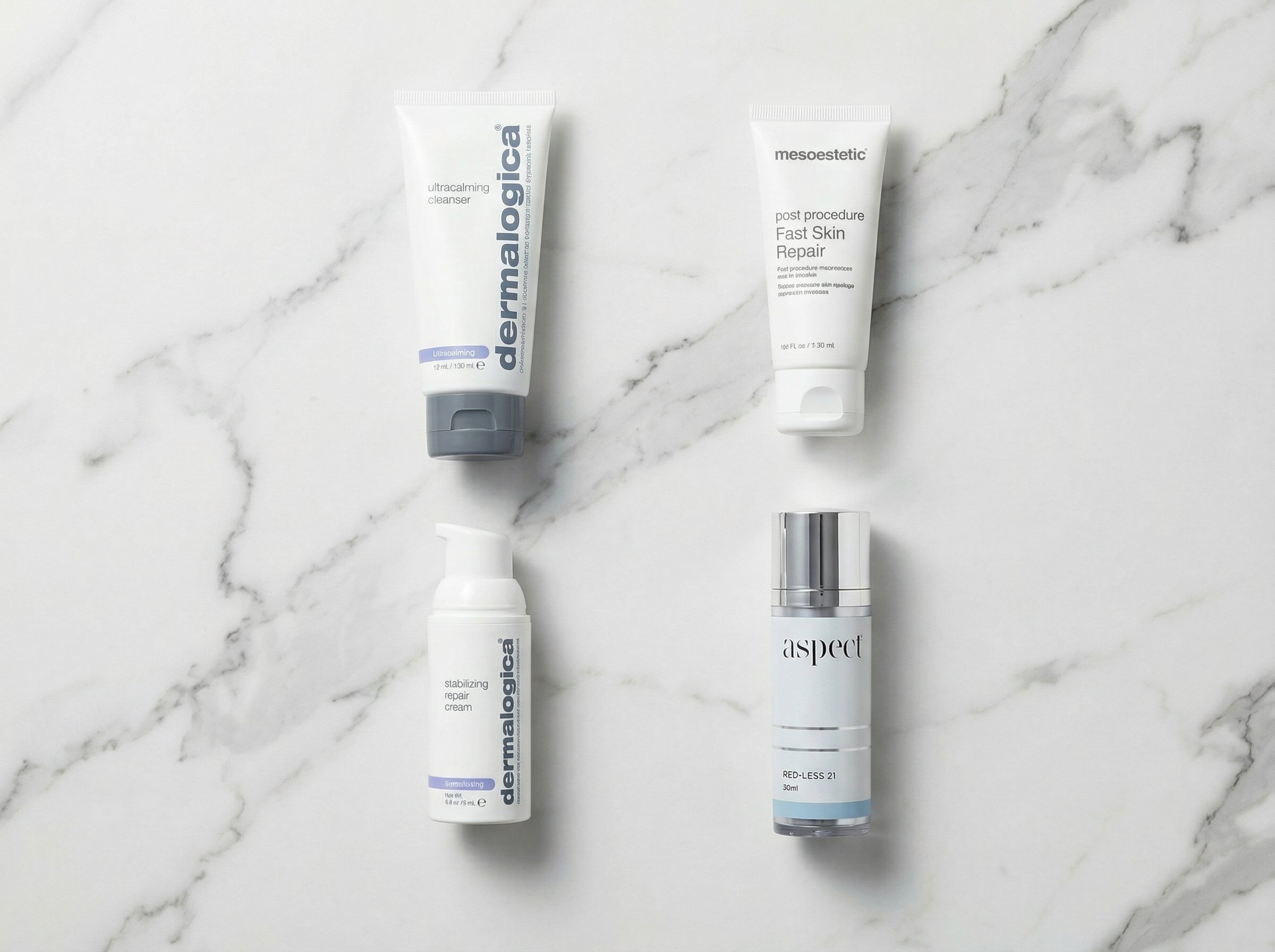 Flat lay of Aspect Red-Less 21, Dermalogica Ultracalming Cleanser, Mesoestetic Post Procedure Fast Skin Repair, and Dermalogica Stabilizing Repair Cream on a white marble surface with soft studio lighting