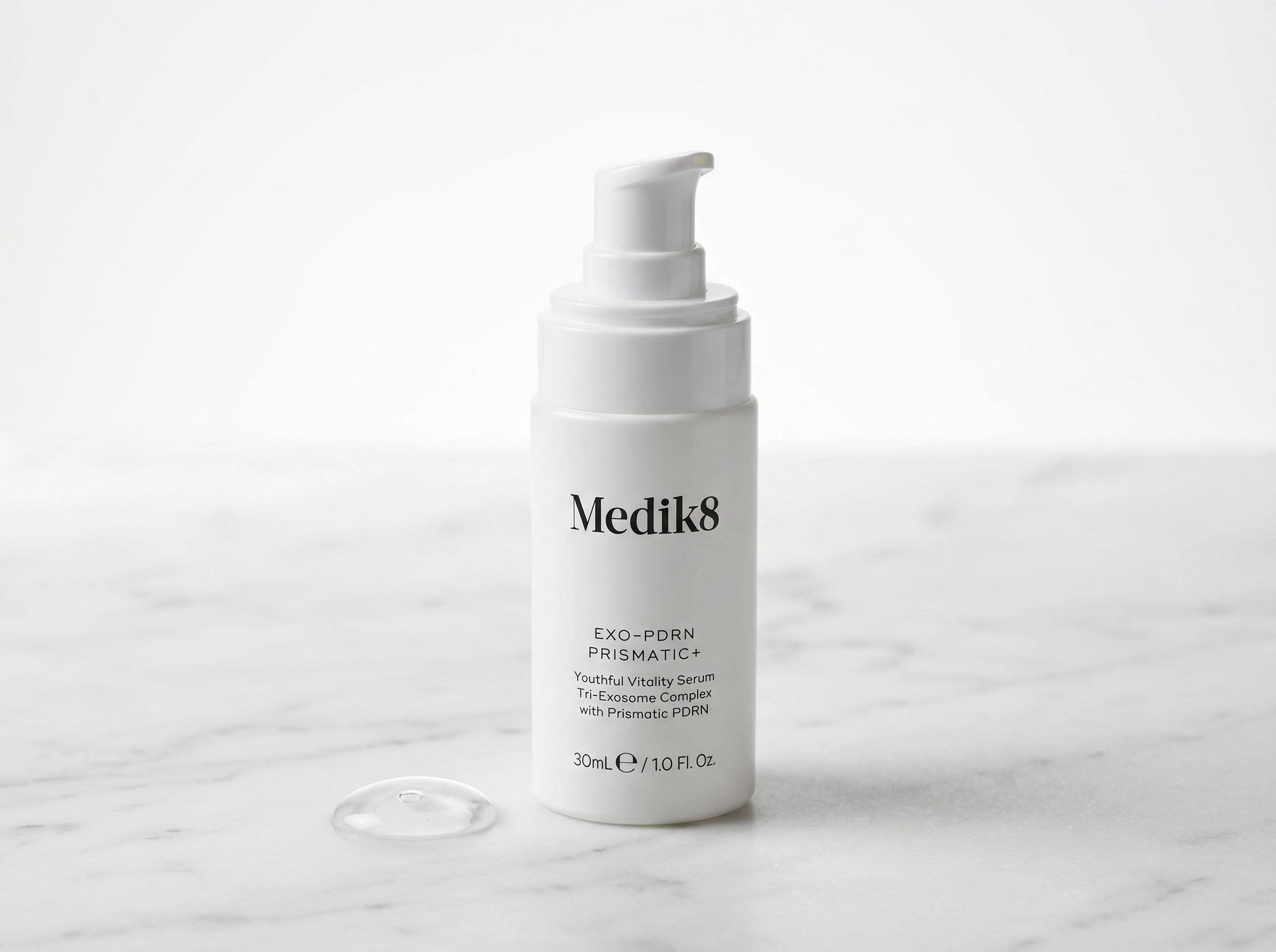 Exo-PDRN Prismatic+ serum bottle on white marble with a dropper of serum suspended above it in soft studio lighting