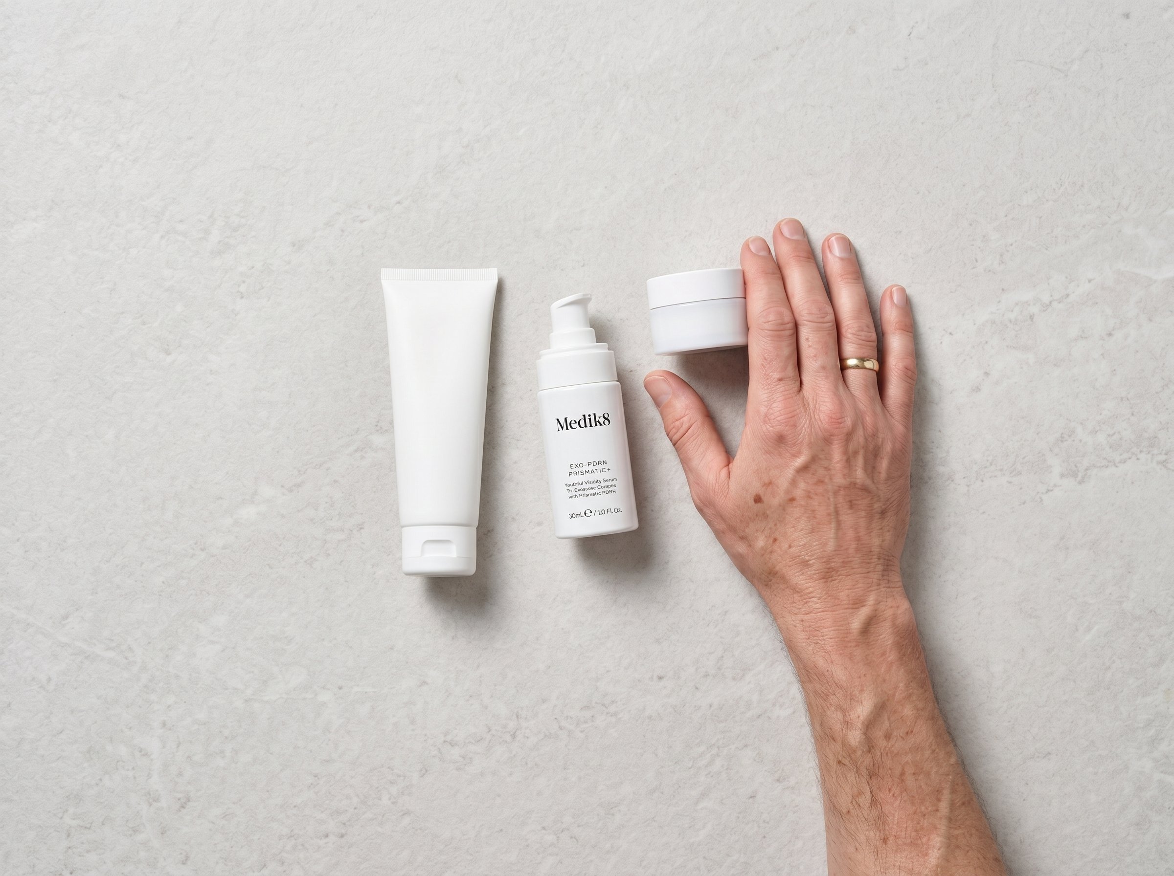 Overhead flat lay of a minimal morning skincare routine including a serum, moisturiser, and sunscreen on a pale stone surface
