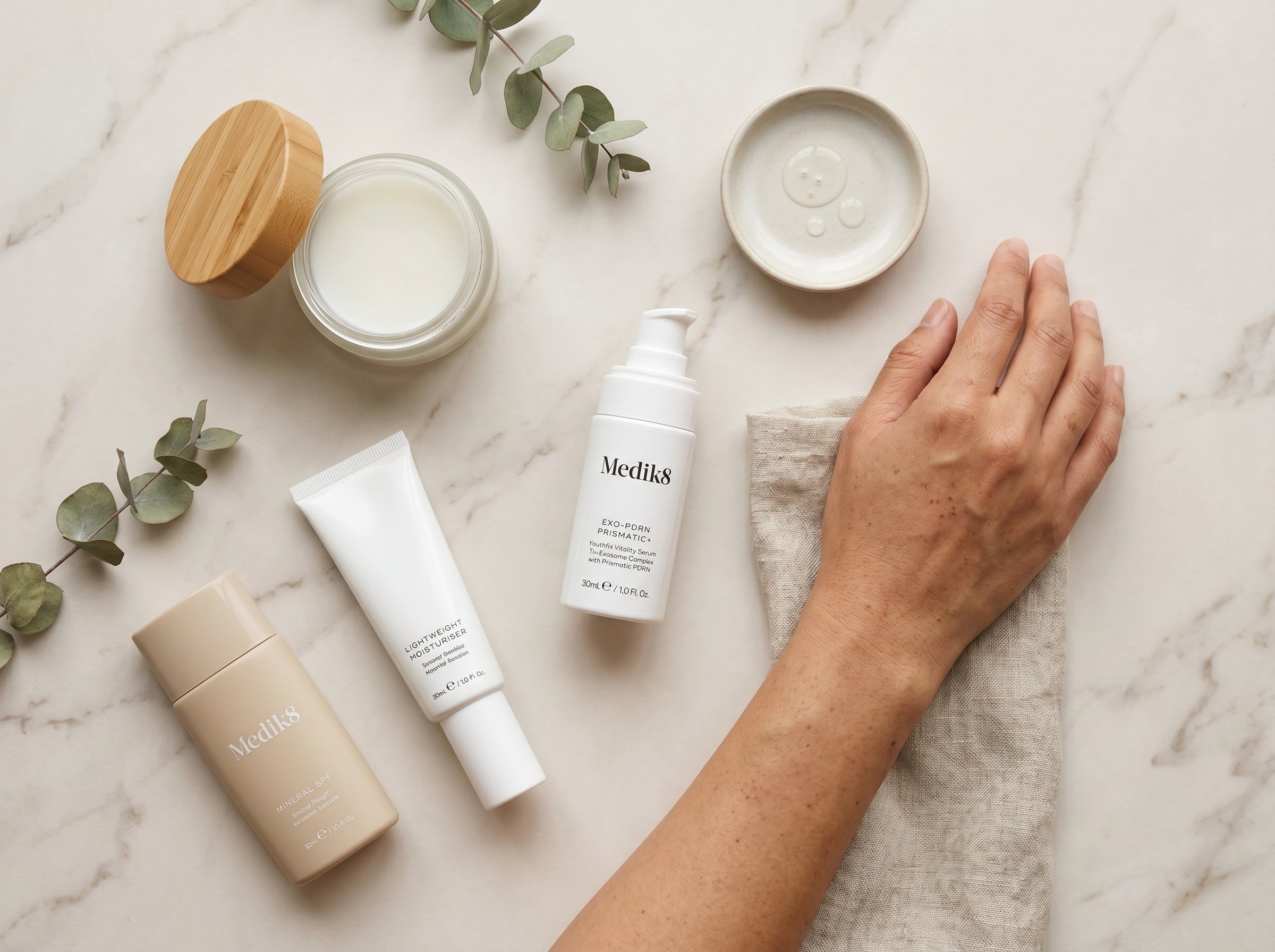 Overhead flat lay of a morning skincare routine including cleanser, Exo-PDRN Prismatic+ serum, moisturiser, and SPF on a light stone surface in soft natural light
