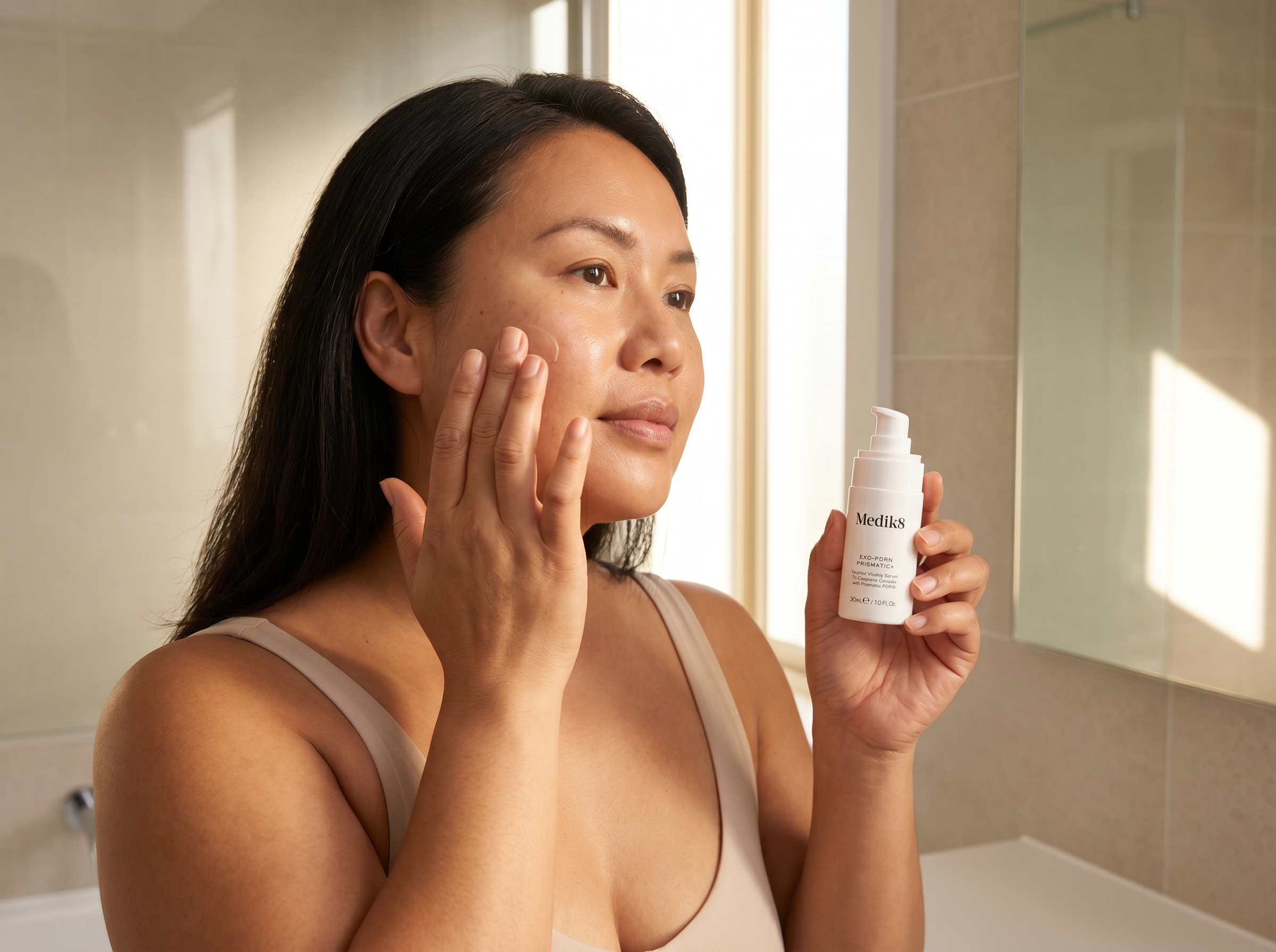 43-year-old East Asian Australian non-binary person with medium skin tone and curvy figure applying face serum in a bright bathroom with natural morning light
