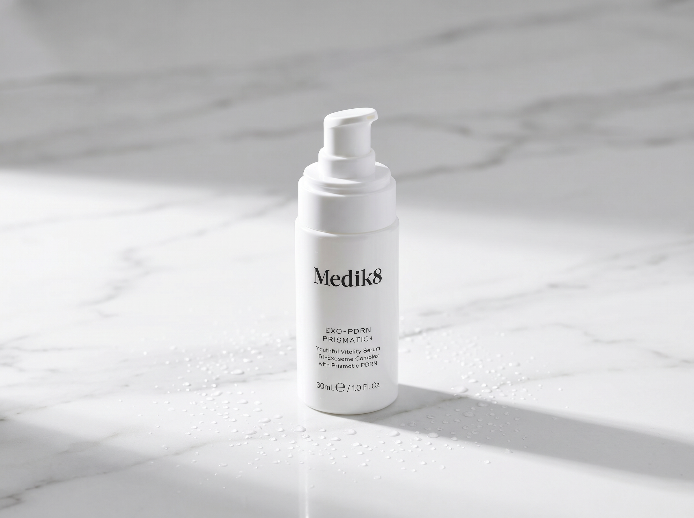 Premium skincare serum bottle on white marble surface with soft directional lighting and small water droplets, editorial product photography style
