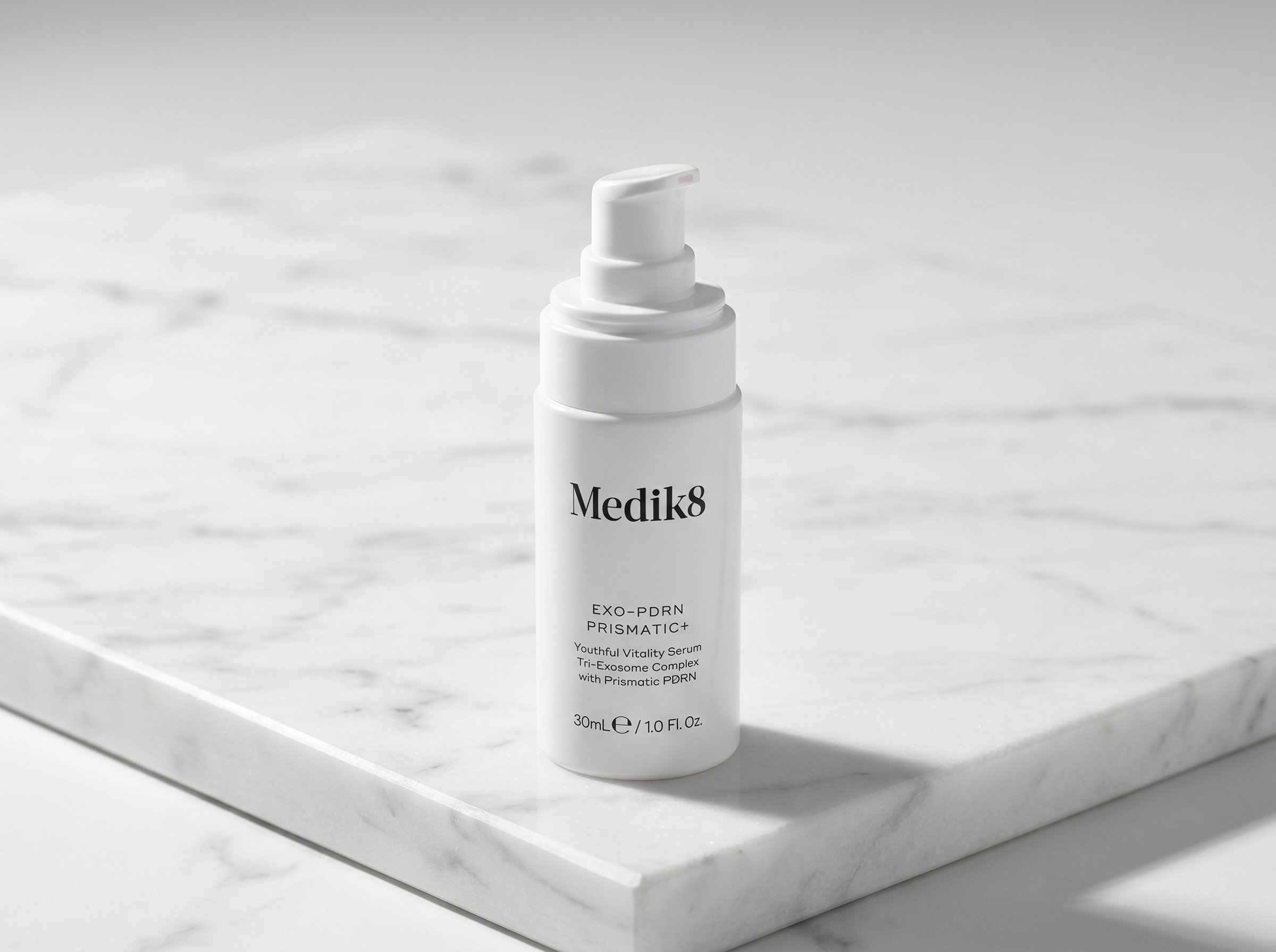 Exo-PDRN Prismatic+ serum bottle on white marble surface with a single dropper of serum beside it