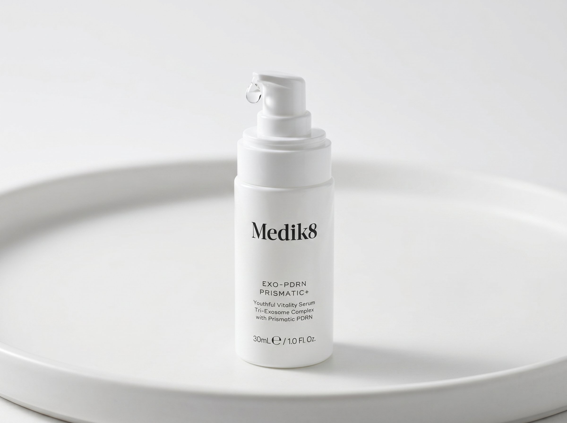 Exo-PDRN Prismatic+ serum bottle with a clear drop on the dropper tip, photographed on a white surface with soft diffused light