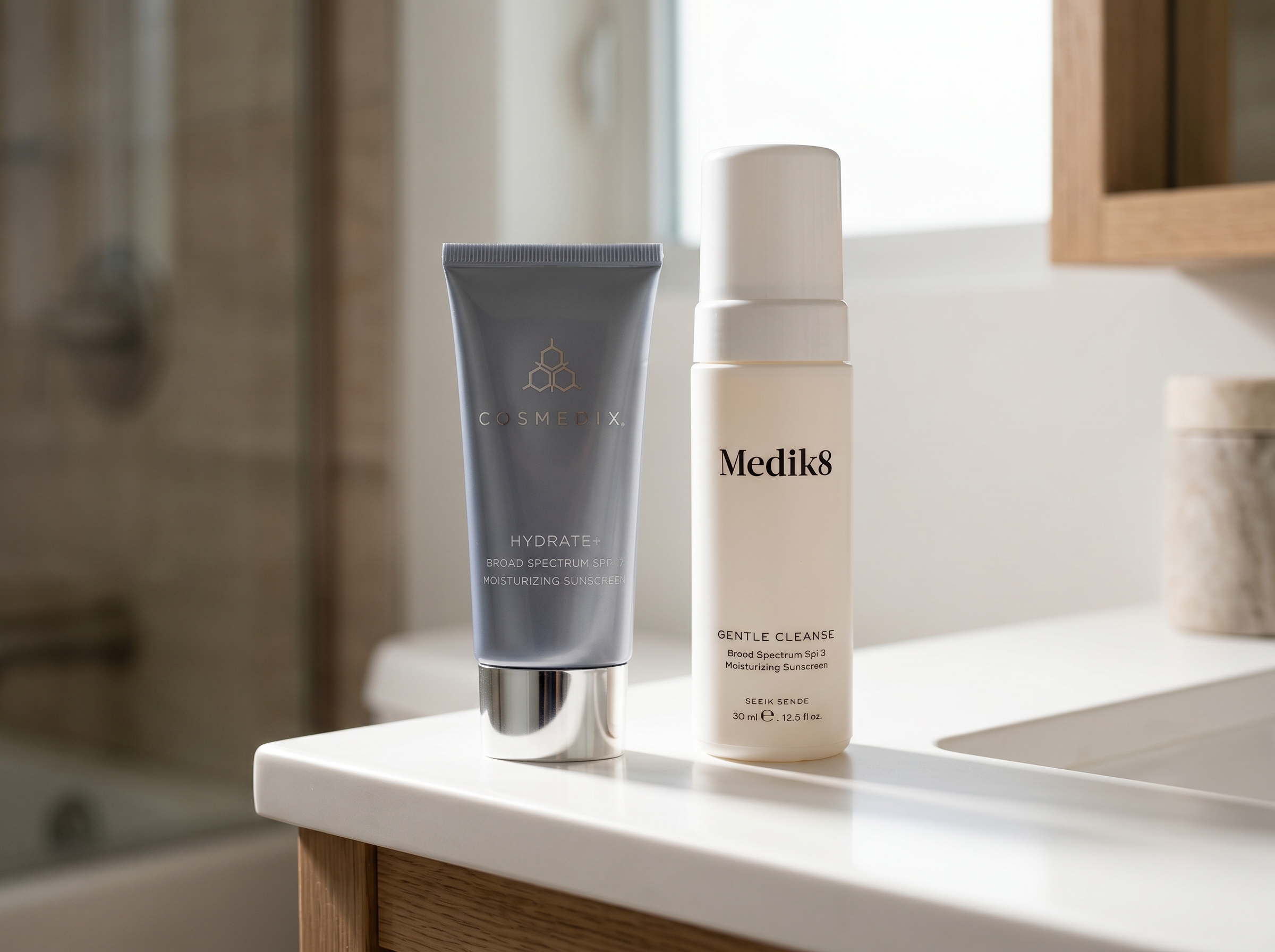 Gentle cleanser and hydrating moisturiser bottles standing on a white counter with soft directional light on their labels