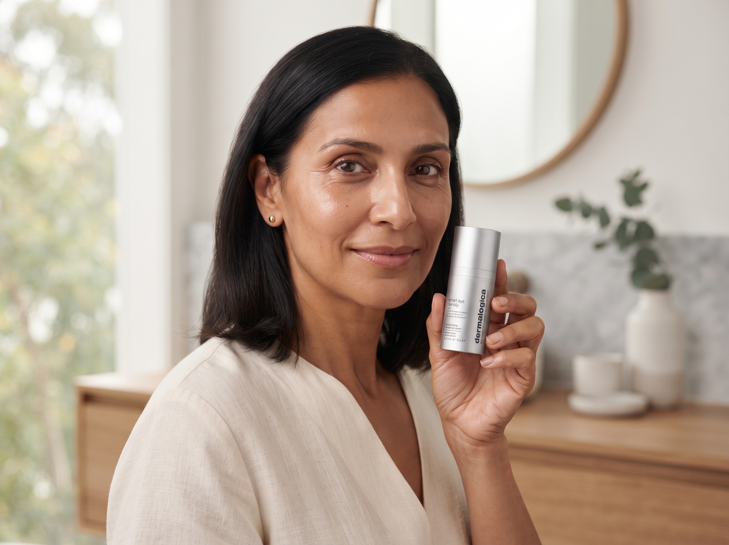Woman holding eye density serum with a calm, confident expression, skin around eyes looking luminous